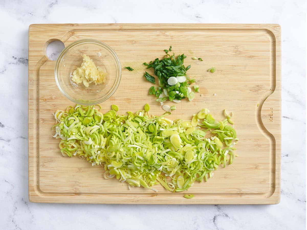 Minced leeks, garlic and green onions on a wooden cutting board.