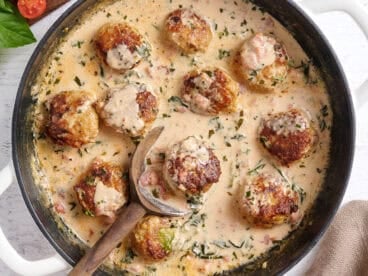 Overhead view of marry meatballs in a skillet with a wooden spoon.