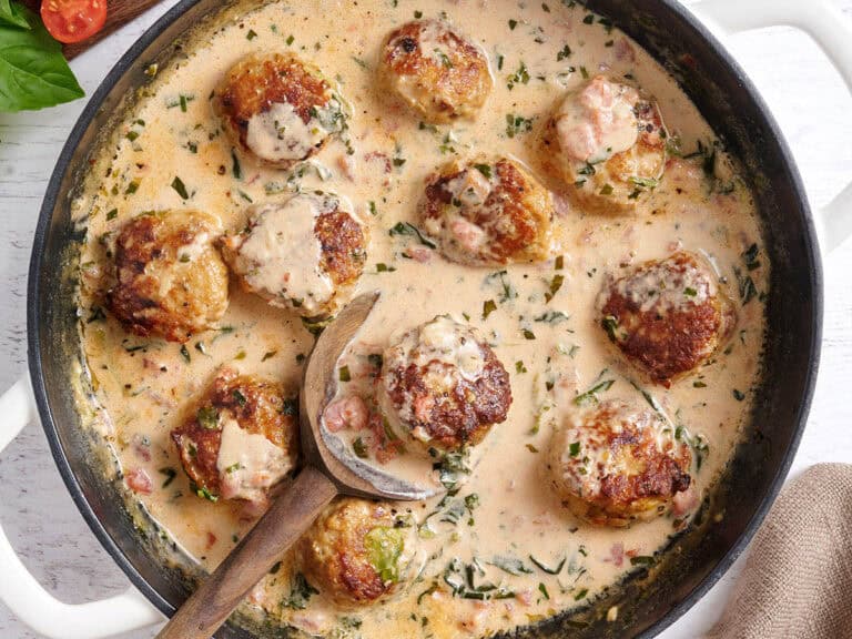 Overhead view of marry meatballs in a skillet with a wooden spoon.