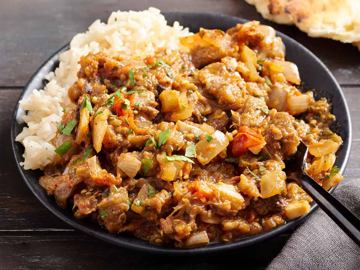 Side view of eggplant curry on a plate with rice.