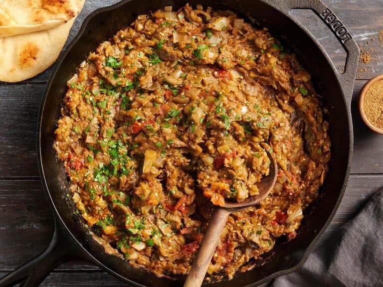 Overhead view of eggplant curry in a skillet with a wooden spoon.