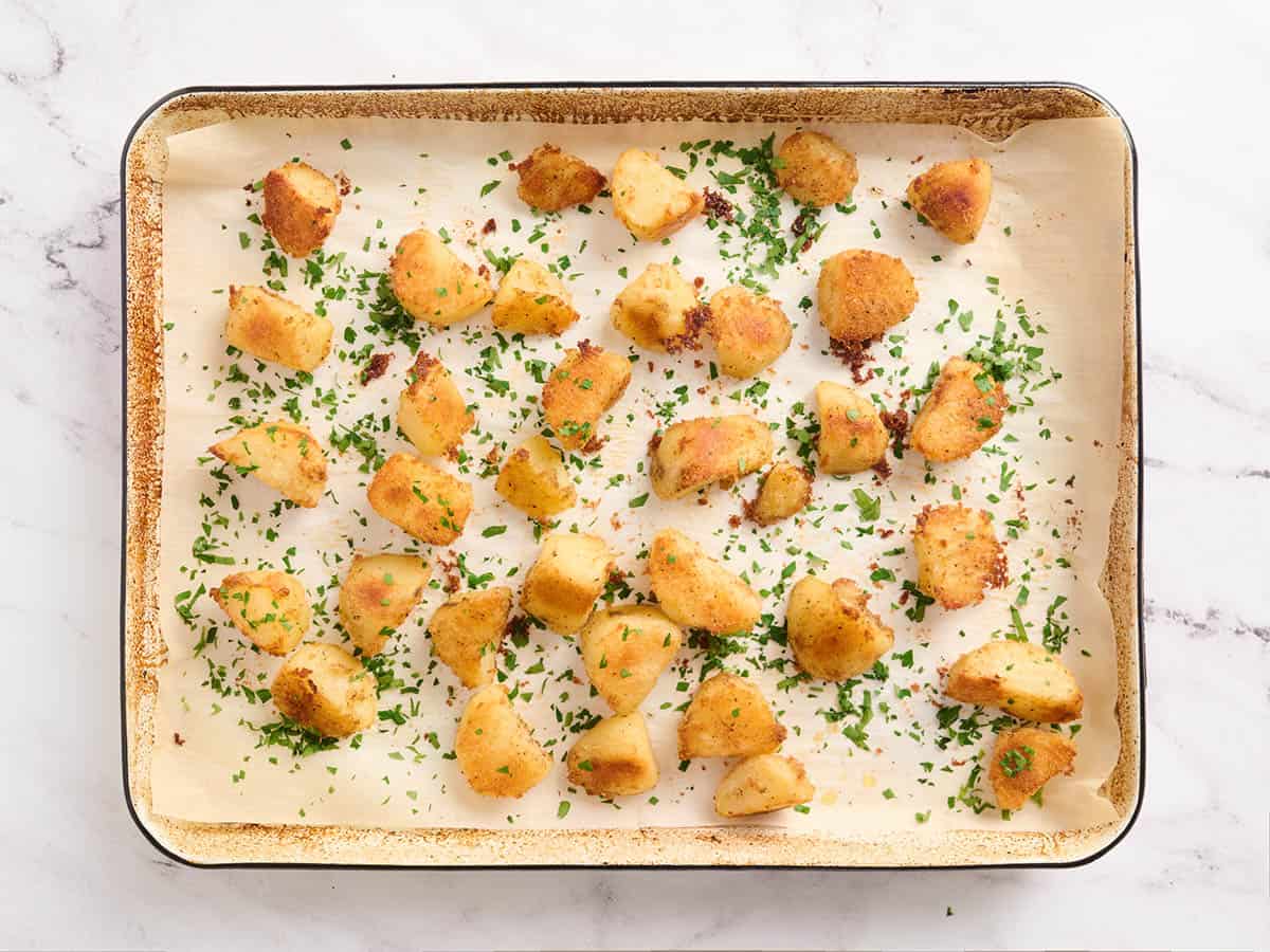 Parsley added to oven roasted potatoes on a baking sheet.