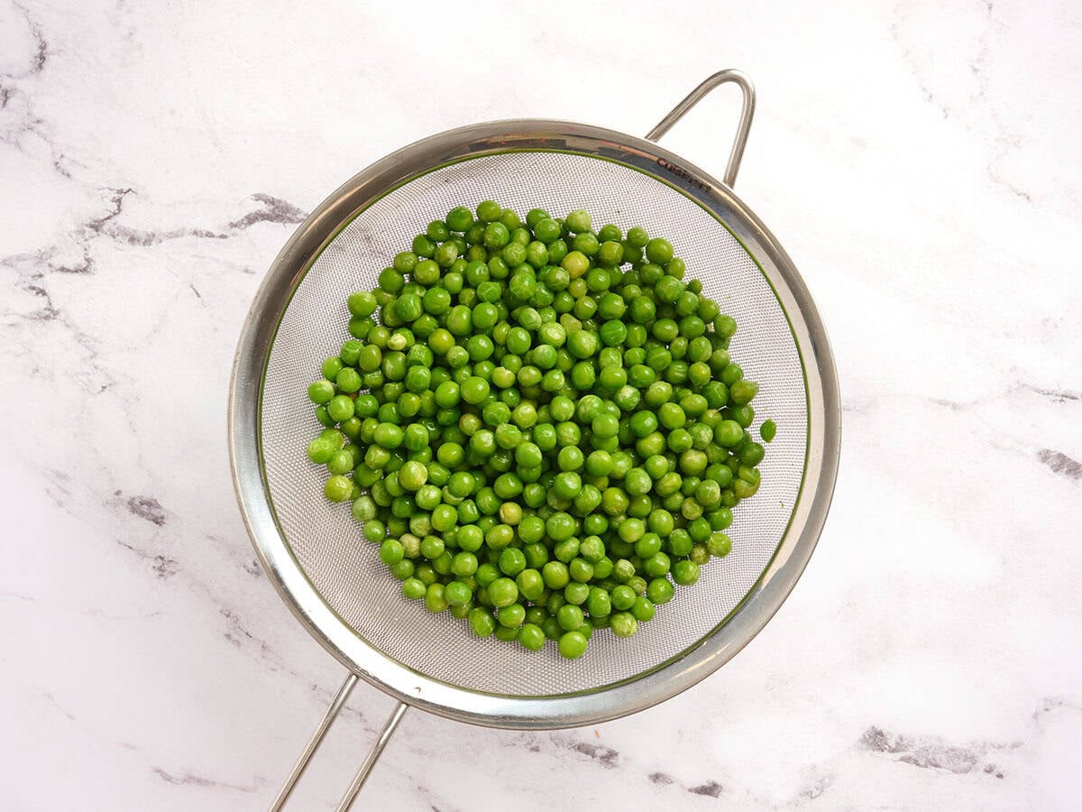 Frozen peas in a sieve.