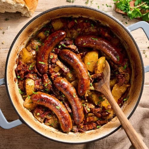Overhead view of dublin coddle in a dutch oven with a wooden spoon.