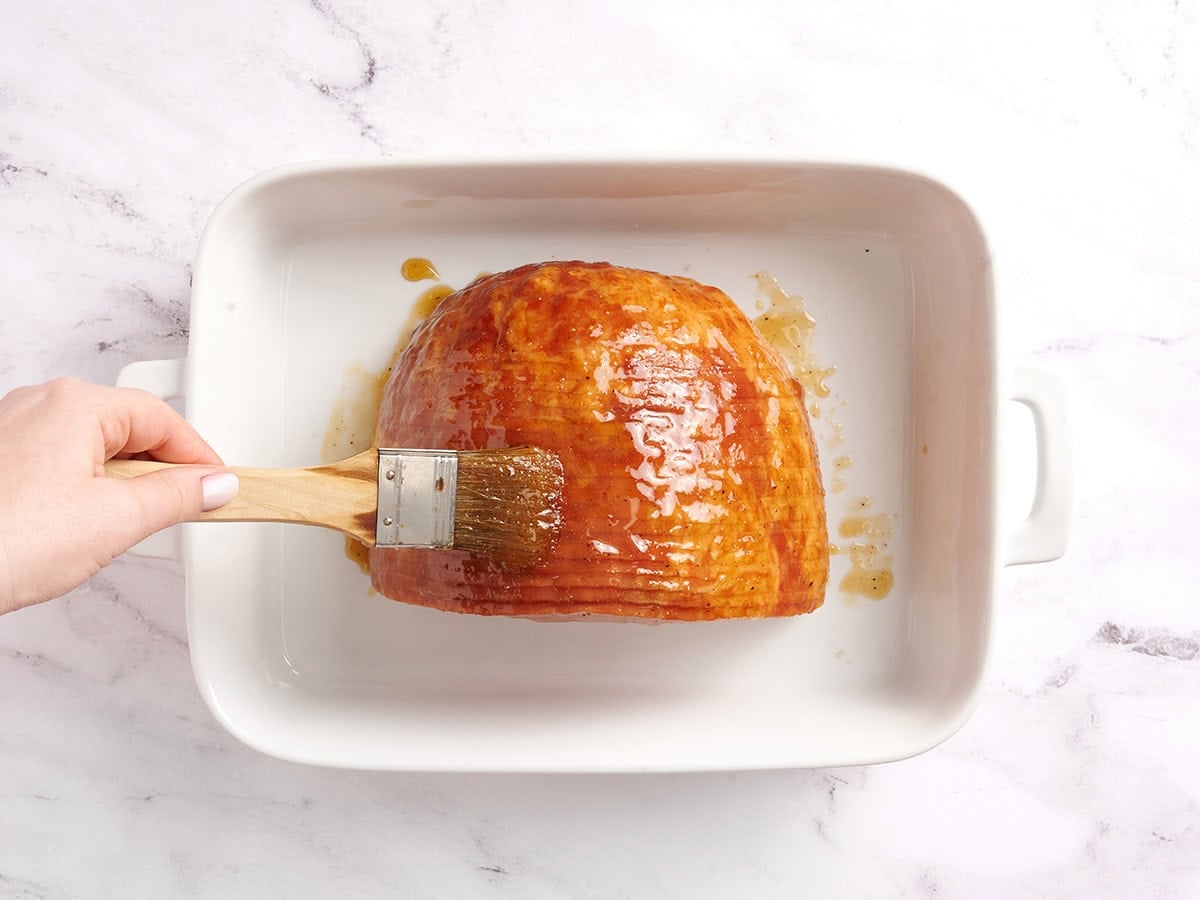 A brush adding honey glaze to a spiral cut ham.