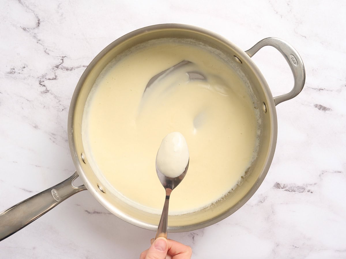 A spoon checking the thickness of a cream sauce in a skillet.