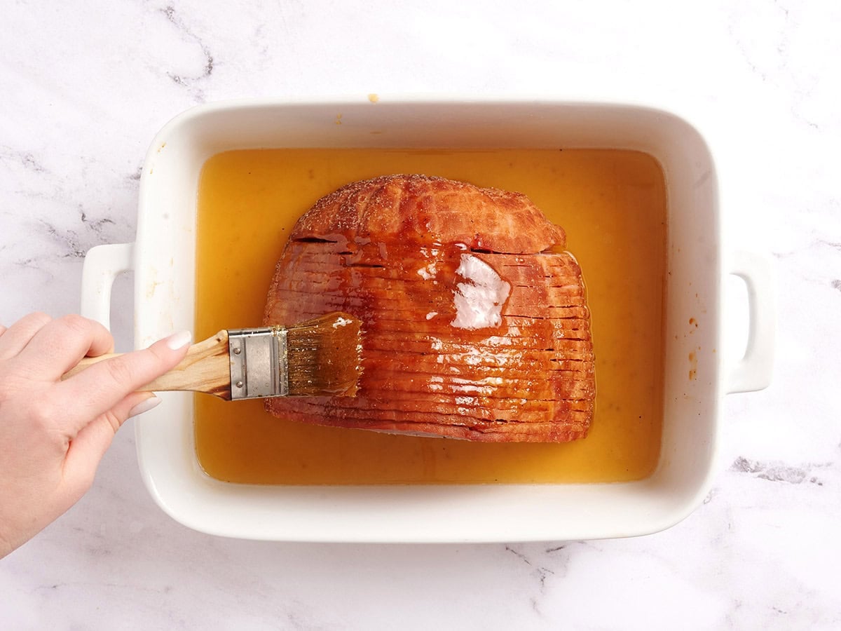 A brush basting a honey glazed ham halfway through cooking.