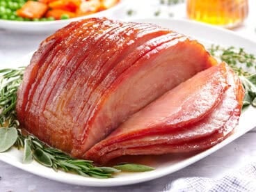 Side view of sliced honey glazed ham on a plate with herbs.