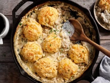 Overhead view of a biscuits and gravy bake in a skillet with a wooden spoon.