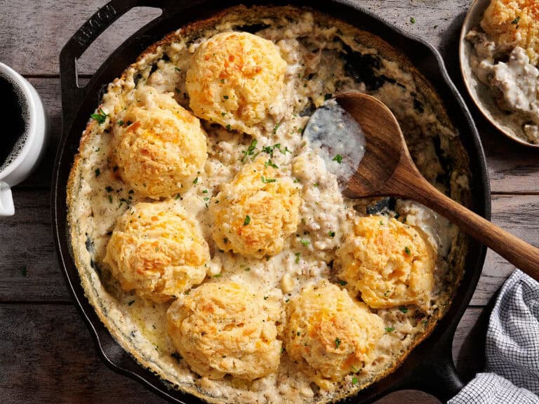 Overhead view of a biscuits and gravy bake in a skillet with a wooden spoon.
