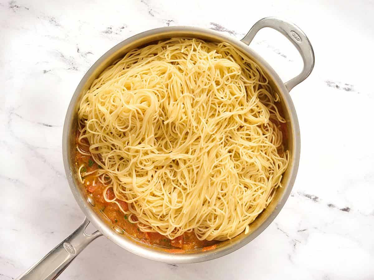 Angel hair pasta added to a skillet with veggies.
