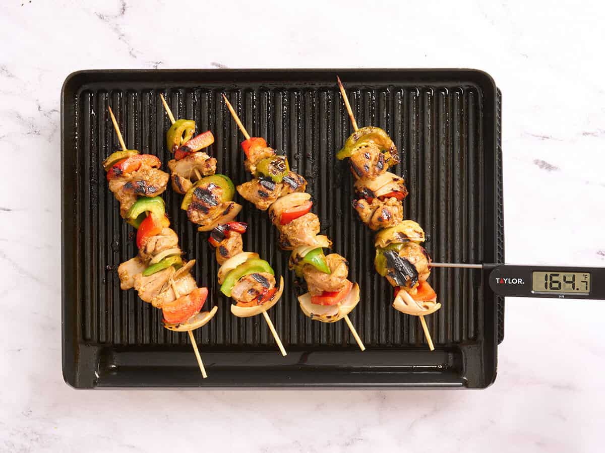 Four chicken kebabs cooking on a grill.