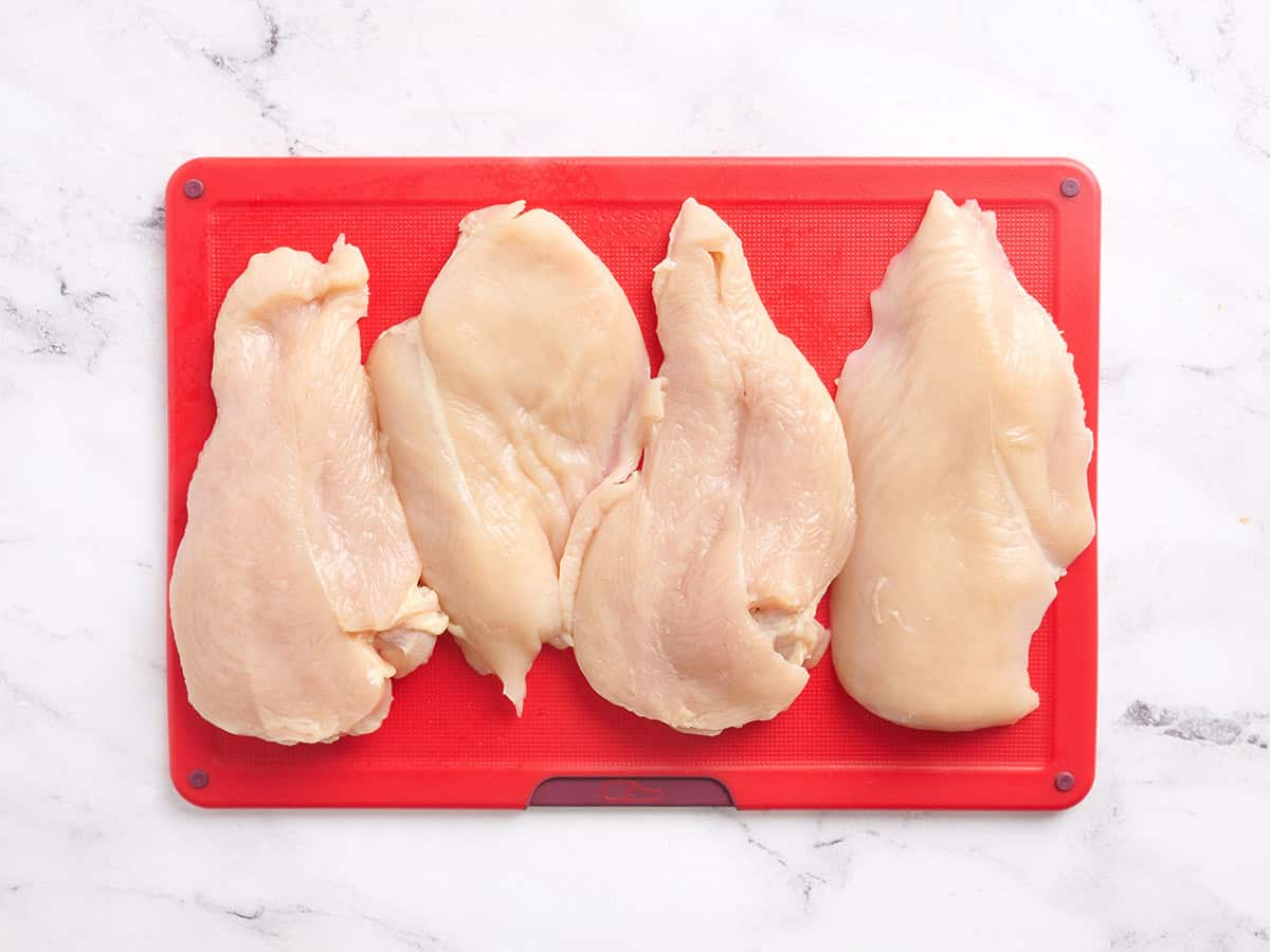 Two filleted chicken breasts on a cutting board.