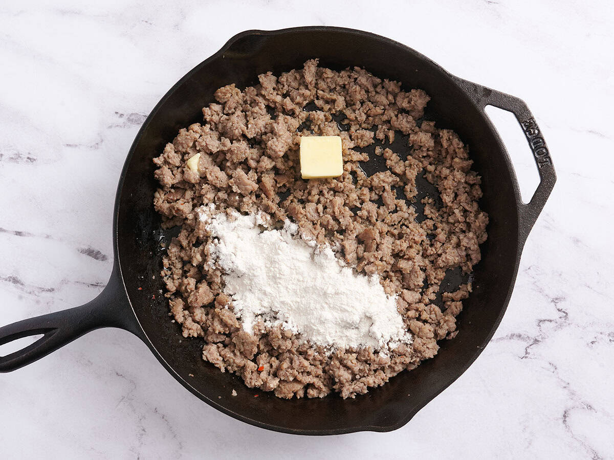 Flour and butter added to browned sausage meat in a skillet.