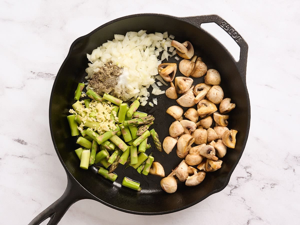 Mushrooms, asparagus, and onions in a cast iron skillet.