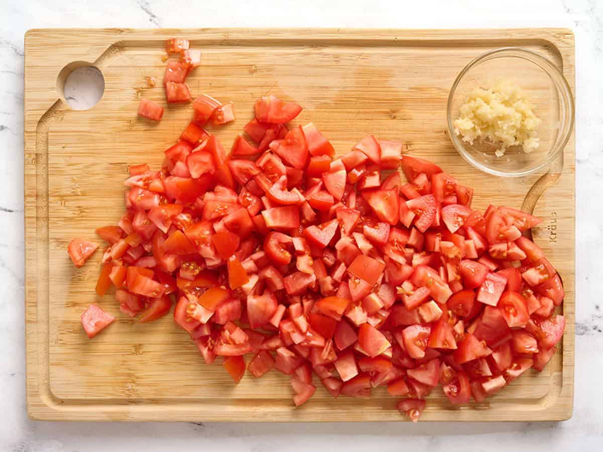 Diced roma tomatoes and minced garlic on a cutting board.