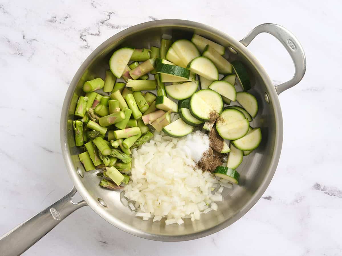 Zucchini, onion, and asparagus in a skillet with seasoning.