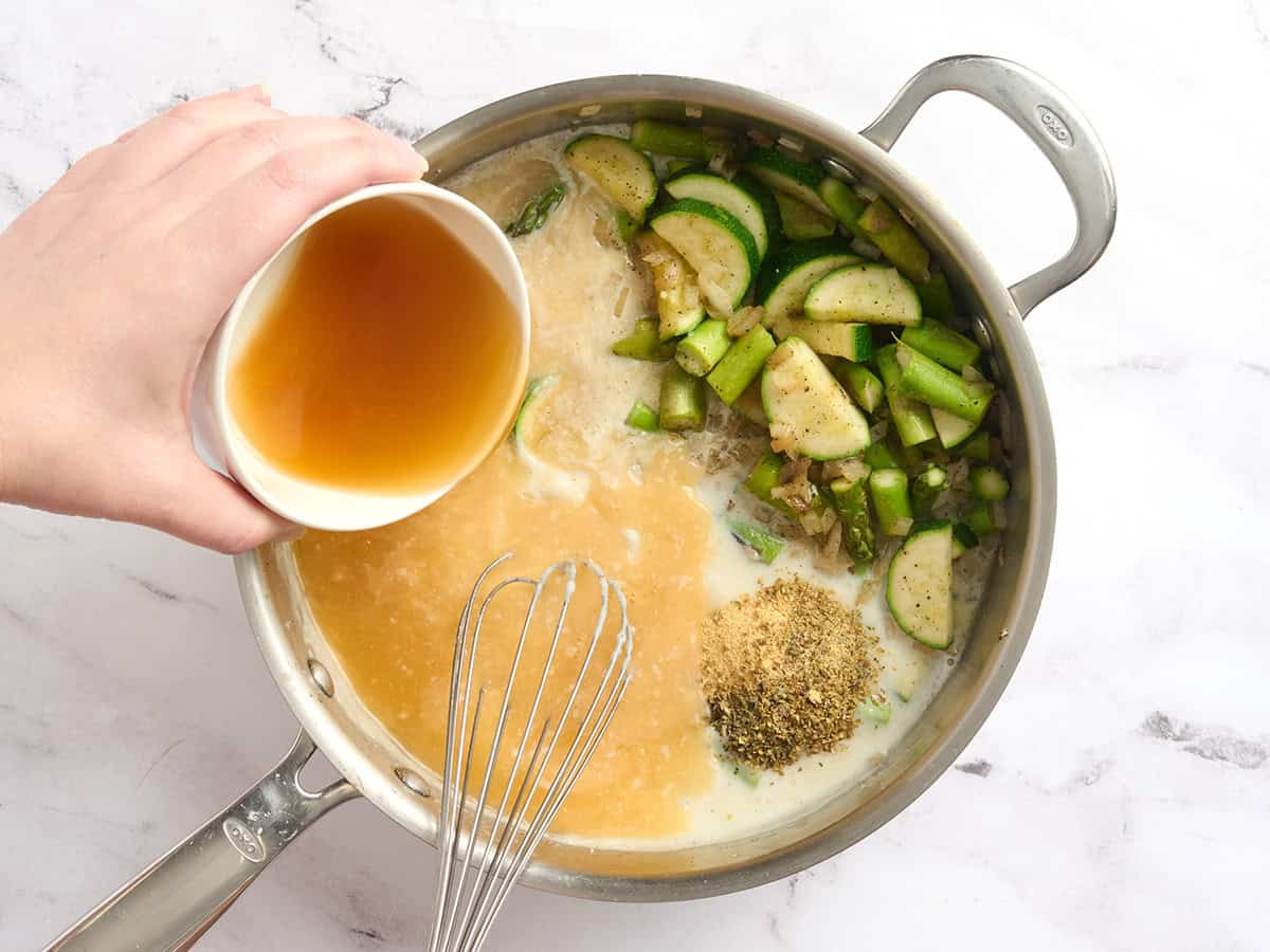 Broth added to a skillet with spring veggies and a thickened milk sauce.