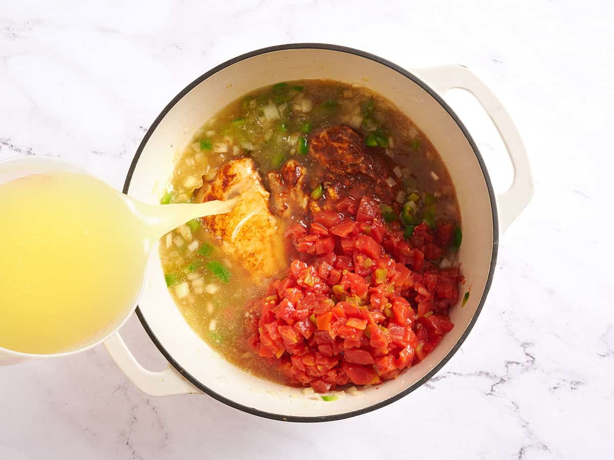 Canned tomatoes with chilies, chicken breasts, and onions in a pot with chicken broth being poured in.