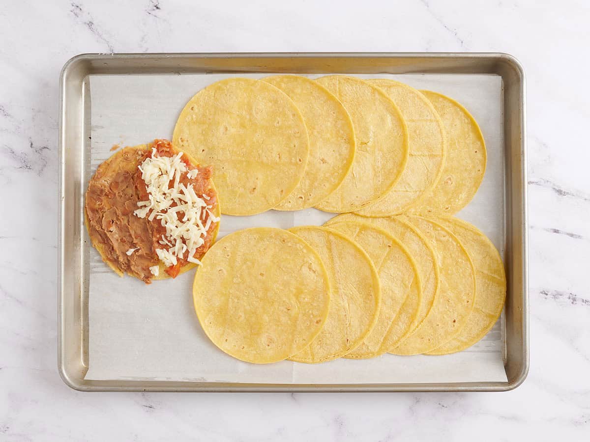 A tortilla with turkey and refried beans topped with shredded cheese before baking.