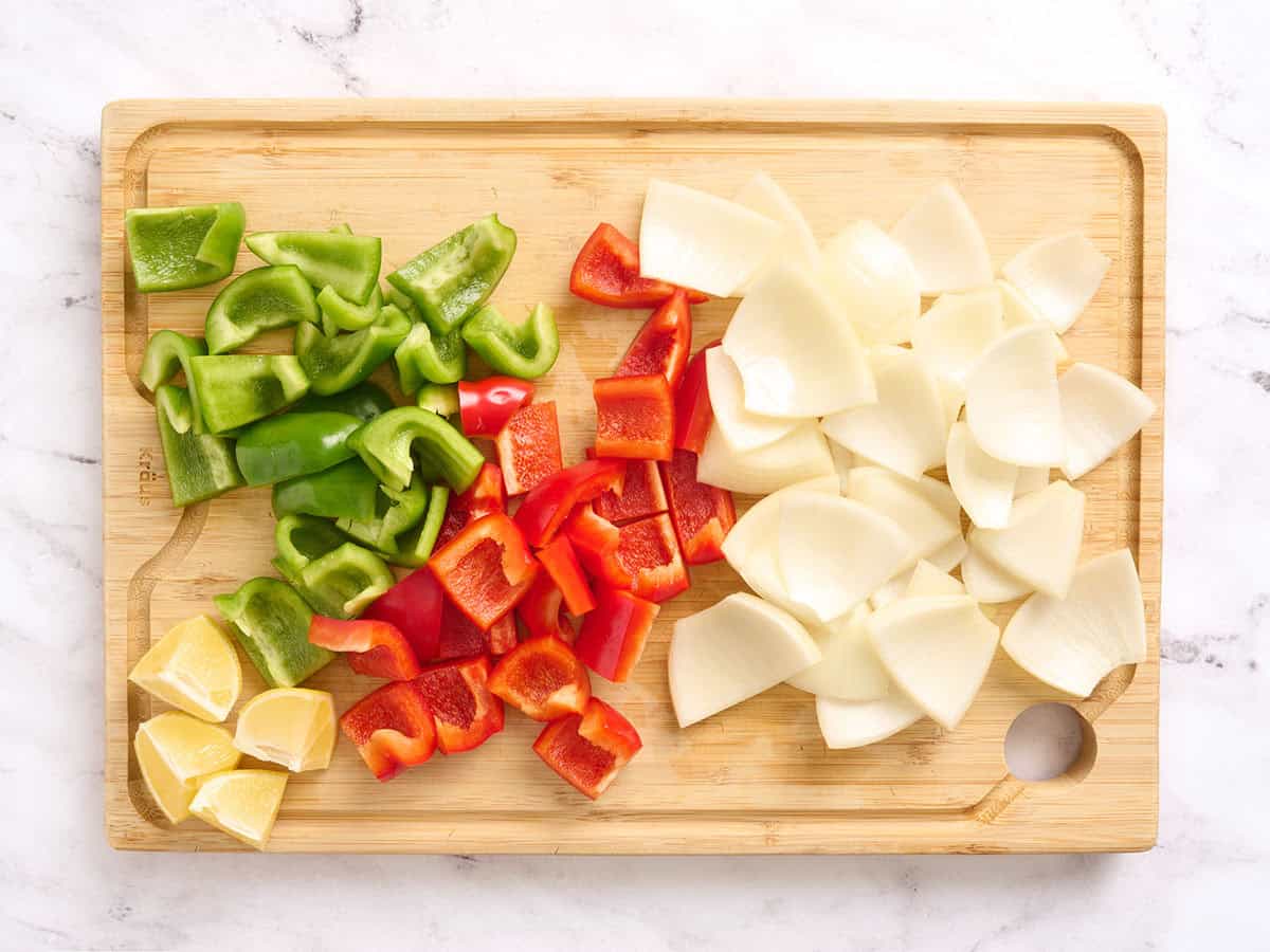 Diced onion, green and red bell peppers and a quartered lemon on a wooden cutting board.