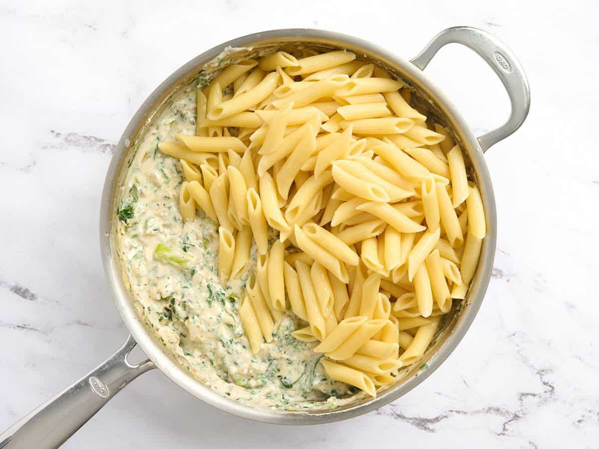 Pasta added to a creamy sauce and veggies in a skillet.