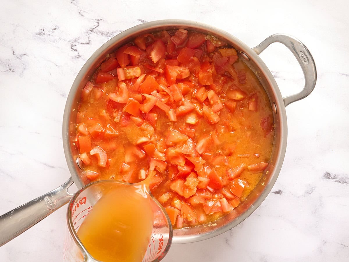 Broth added to tomatoes in a skillet.