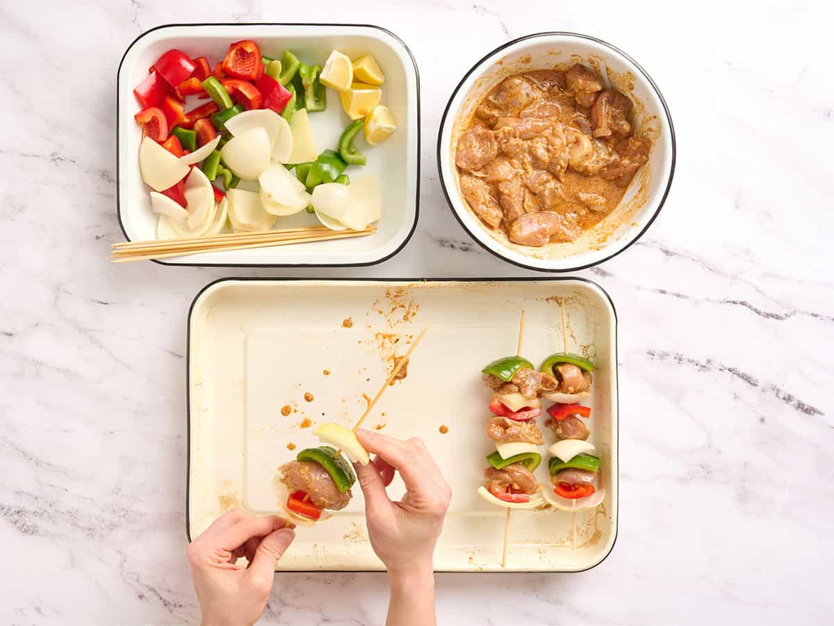 A hand threading bell pepper, onion and chicken onto a skewer.