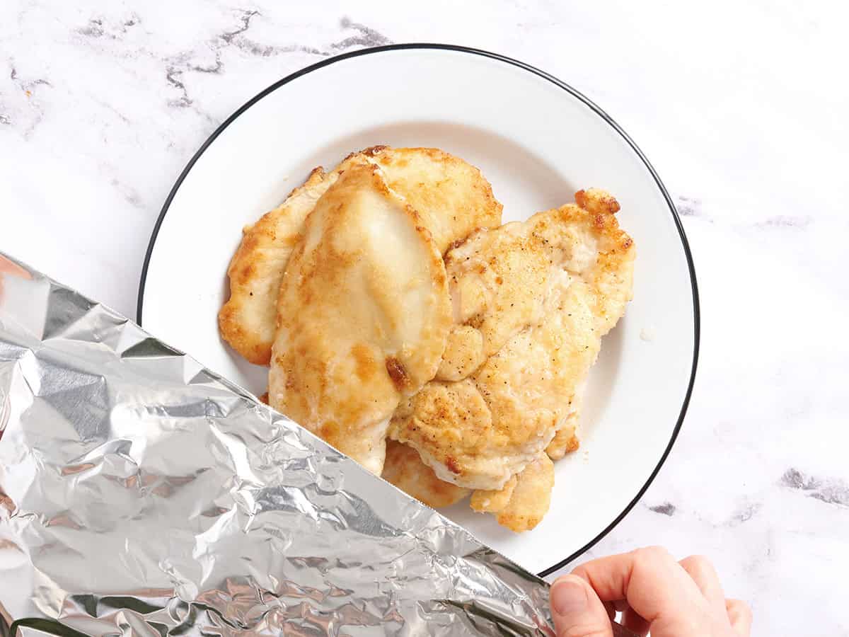 Hands covering cooked chicken with foil.