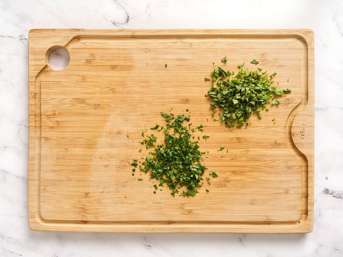 Minced parsley and basil on a wooden cutting board.