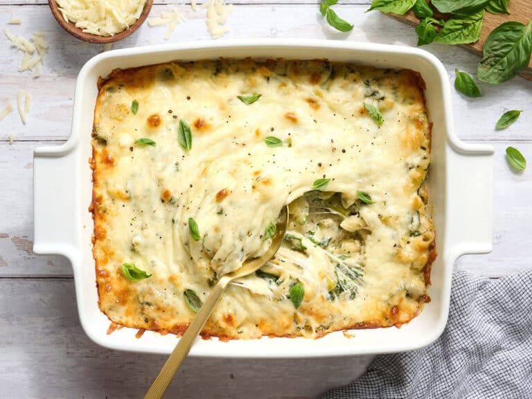 Overhead view of a casserole dish of baked pasta with spring veggies and a spoon.