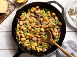 Overhead view of gnocchi with spring vegetables in a skillet with a wooden spoon.