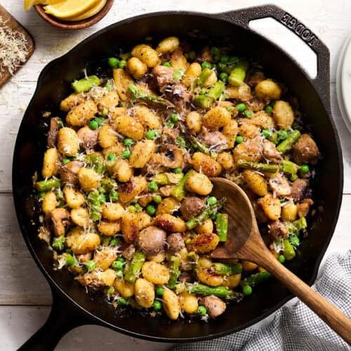 Overhead view of gnocchi with spring vegetables in a skillet with a wooden spoon.