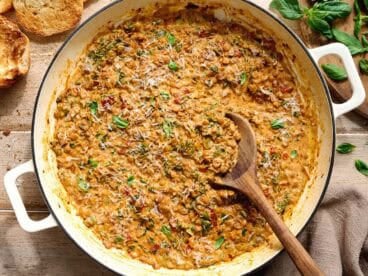 Overhead view of marry me lentils in a skillet with a wooden spoon.