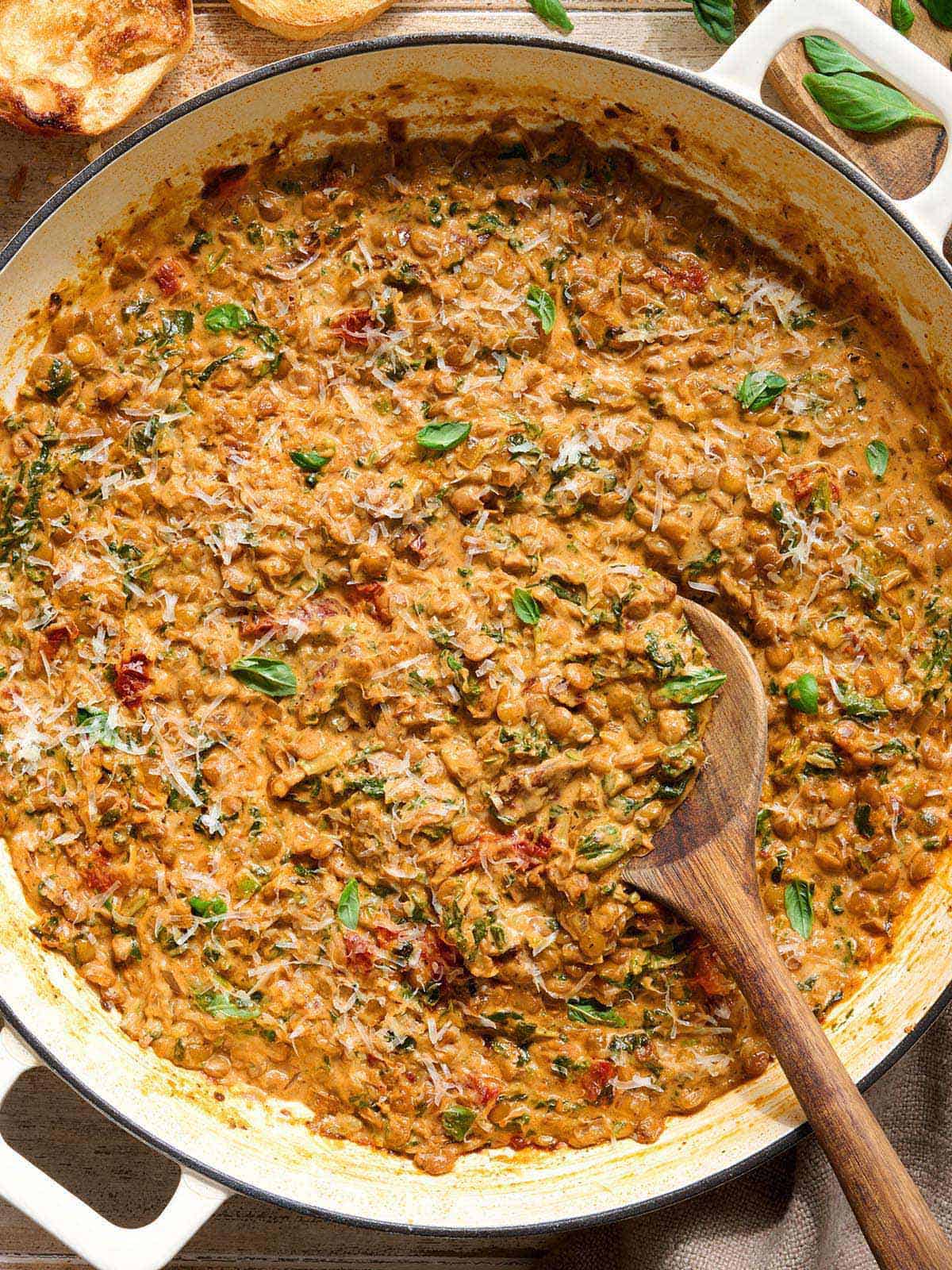 Overhead view of marry me lentils in a skillet with a wooden spoon.