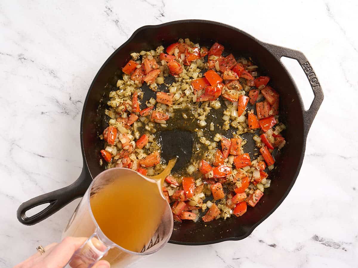 Vegetable broth added to a skillet with onions and tomatoes.