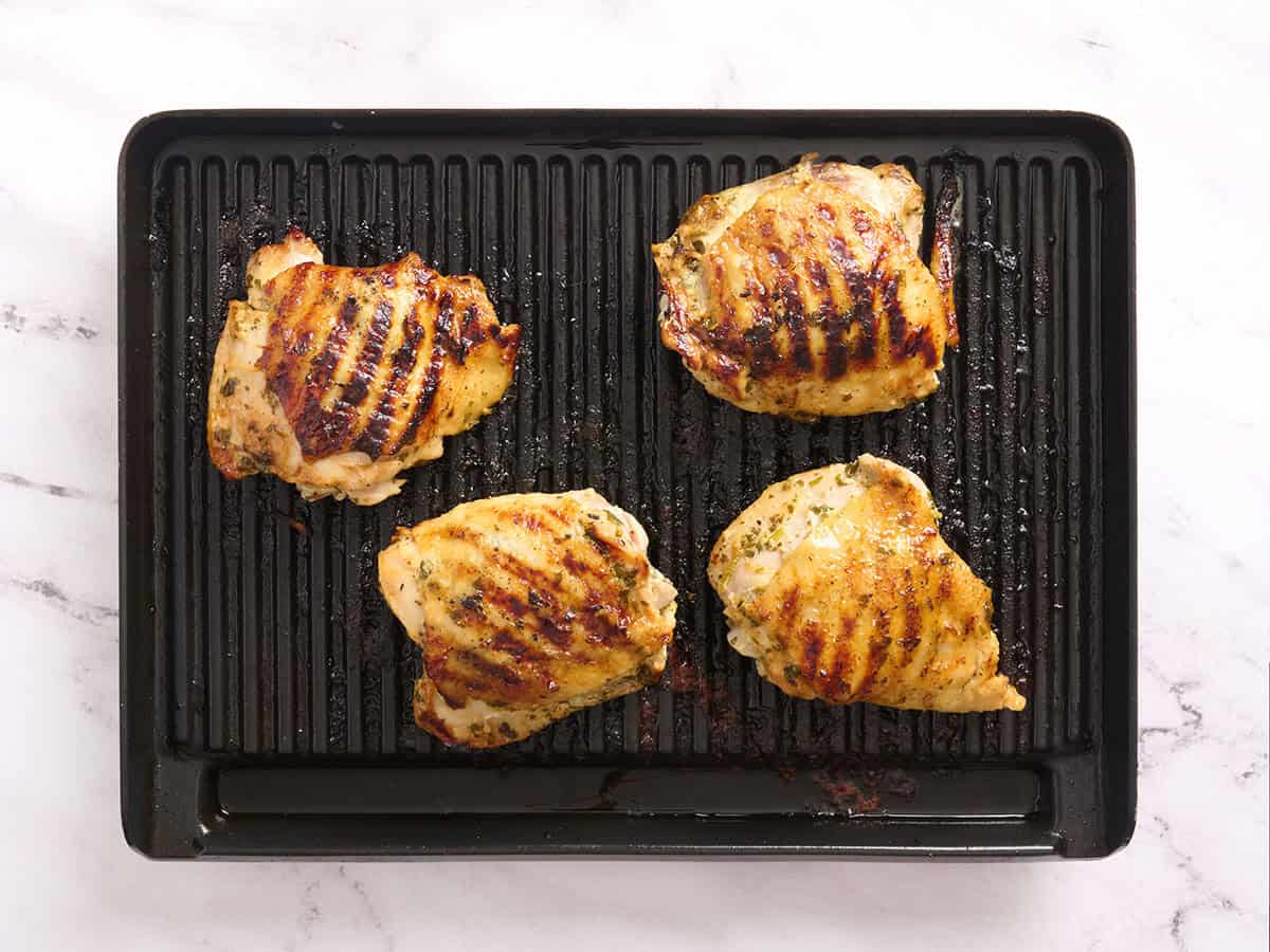 Chicken thighs cooking on a grill.