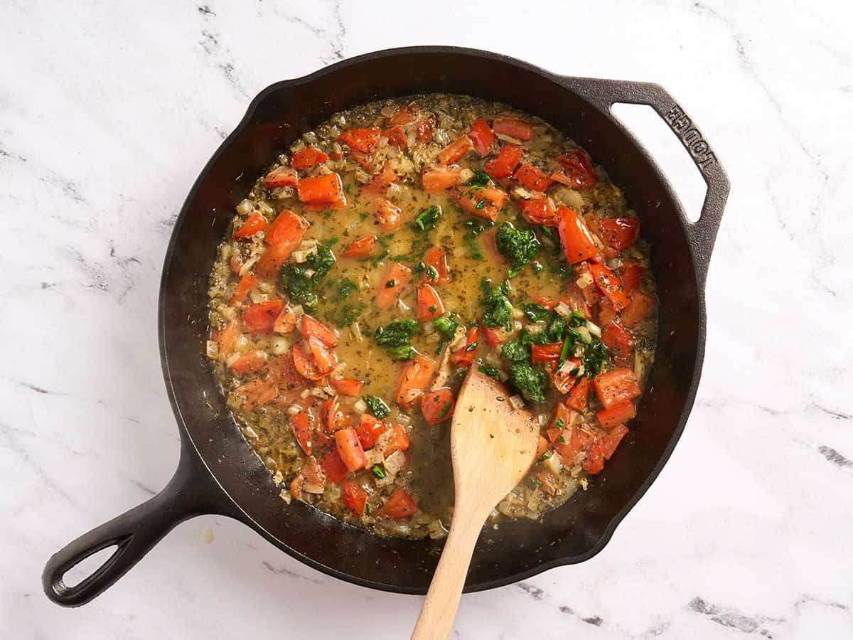 Frozen spinach added to a skillet with tomatoes, onions and broth.