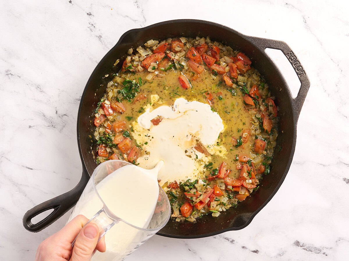 Heavy cream added to a skillet with onions, tomatoes and spinach.