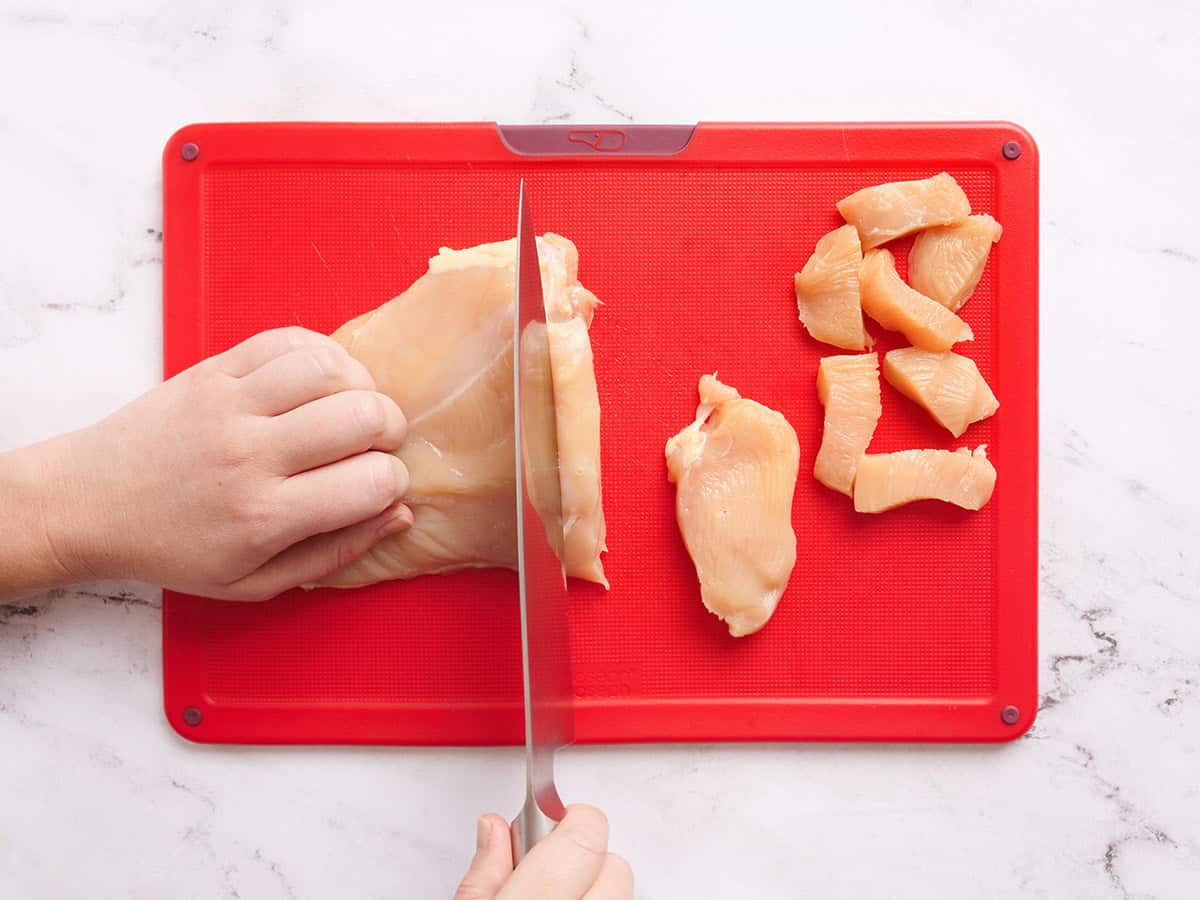Hands using a knife to slice a chicken breast into pieces.