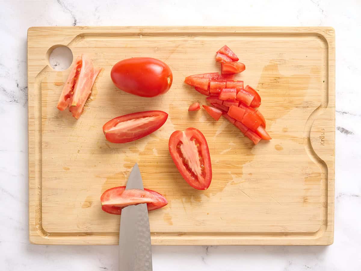 Sliced quartered Roma tomatoes on a wooden cutting board, with a knife removing seeds.