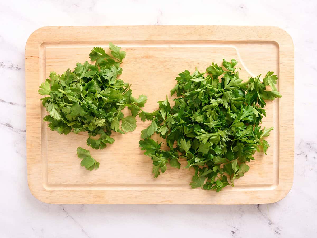 Parsley and cilantro on a wooden cutting board.