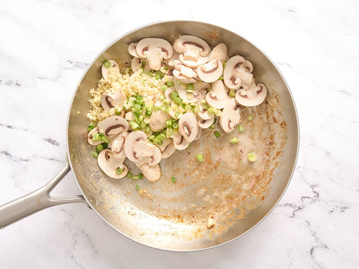 Mushrooms and green onions in a skillet.