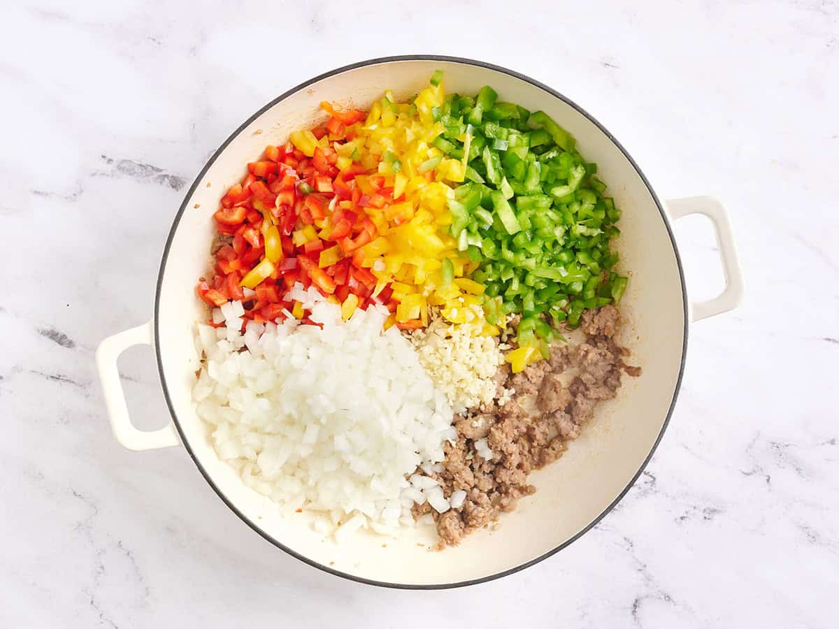 Diced bell peppers, onion, garlic and ground sausage in a skillet.