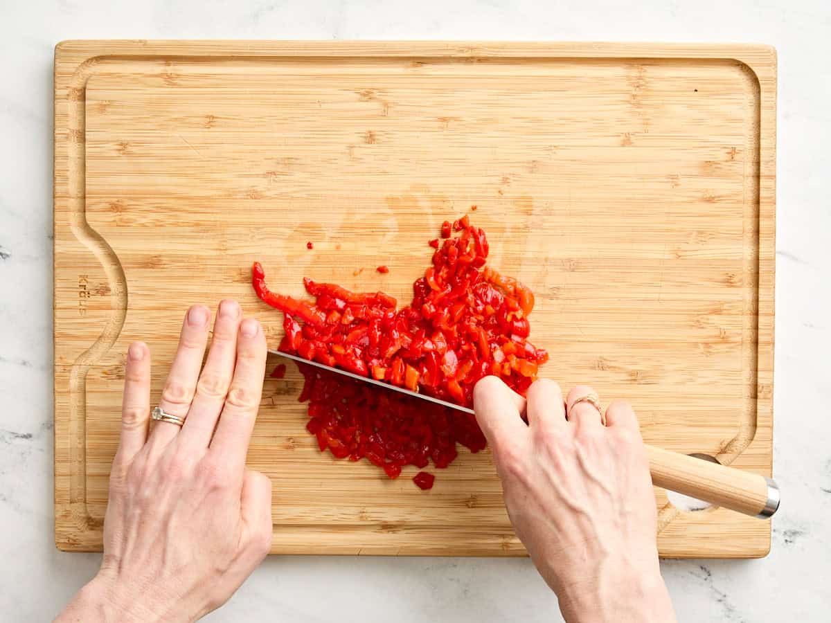 Hands using a knife to mince pimento peppers.