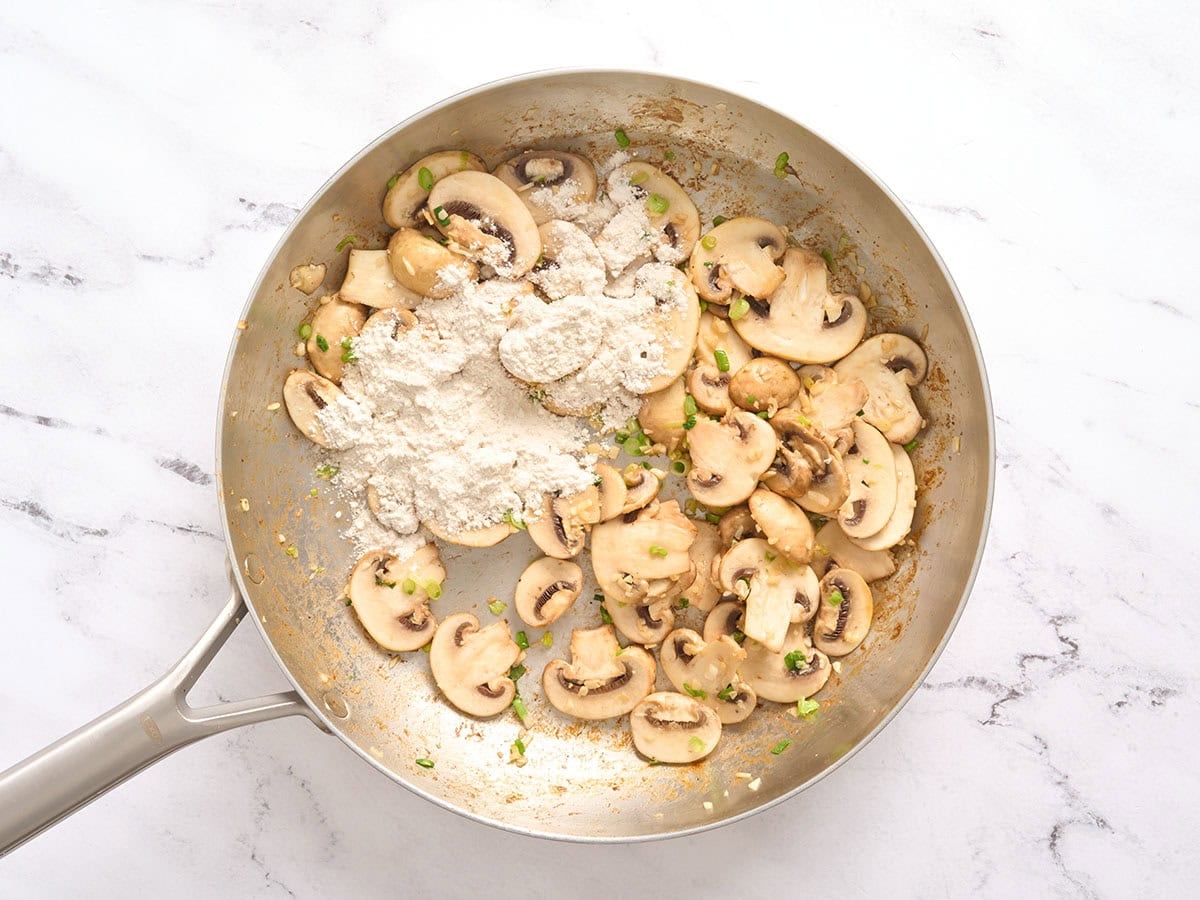 Flour added to sliced mushrooms in a skillet.