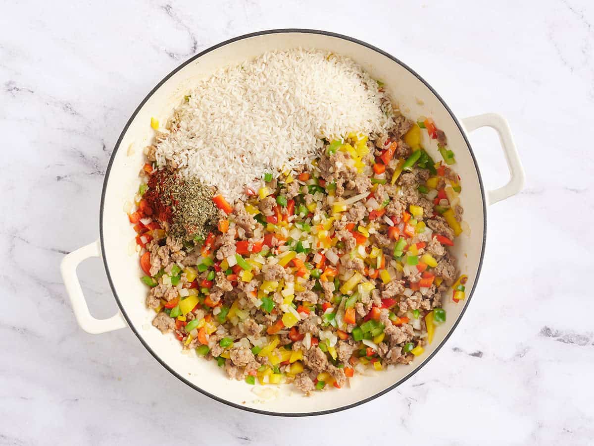 Rice and seasonings added to a skillet with sauteed veggies.
