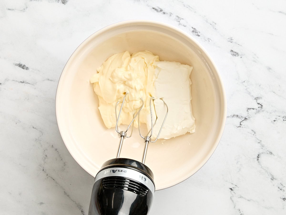 Mayo and cream cheese in a bowl with a hand mixer.