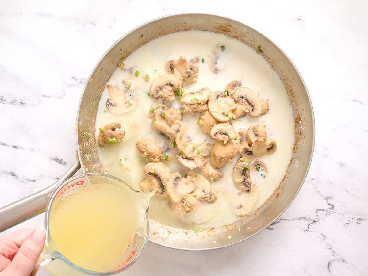 Chicken broth being poured into a killet with mushrooms and milk.
