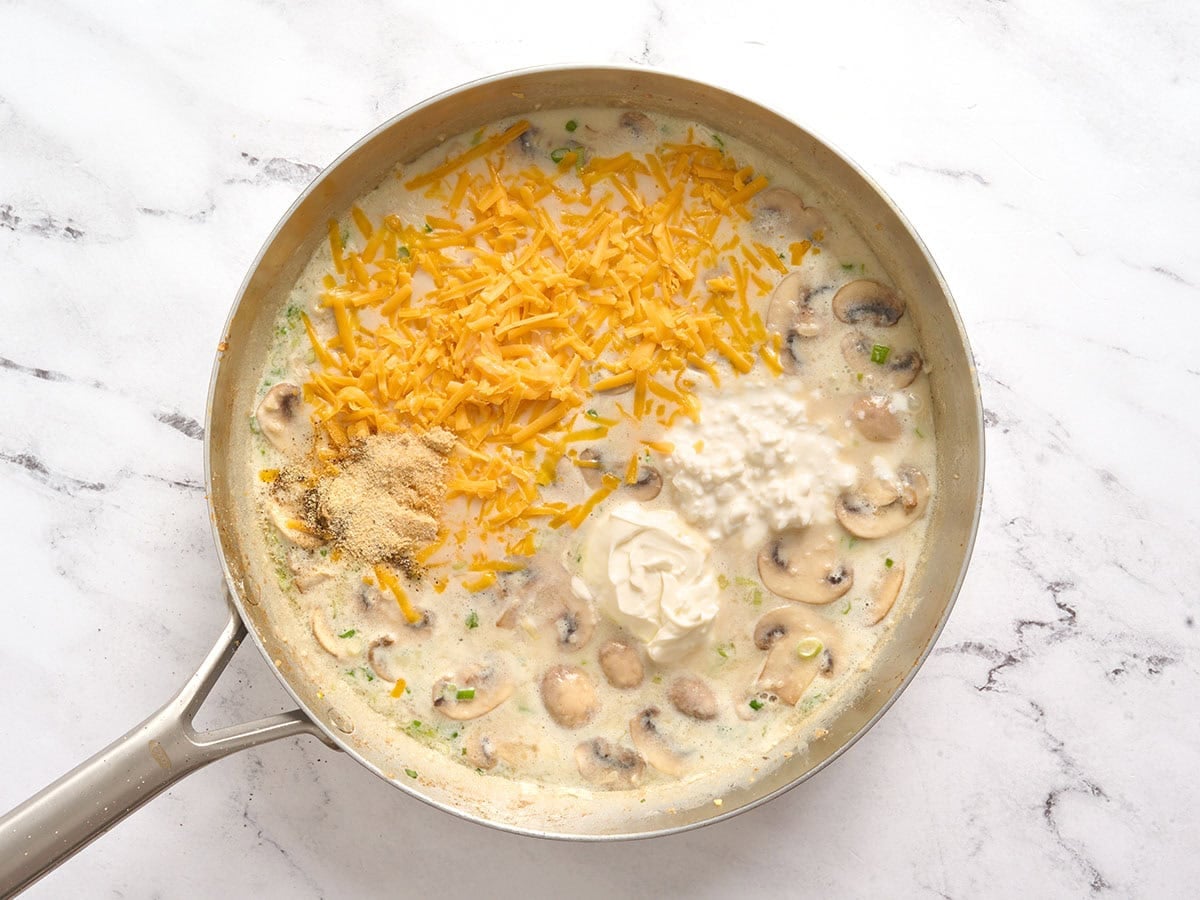 Cheese and spices added to the filling for million dollar chicken casserole in a skillet.